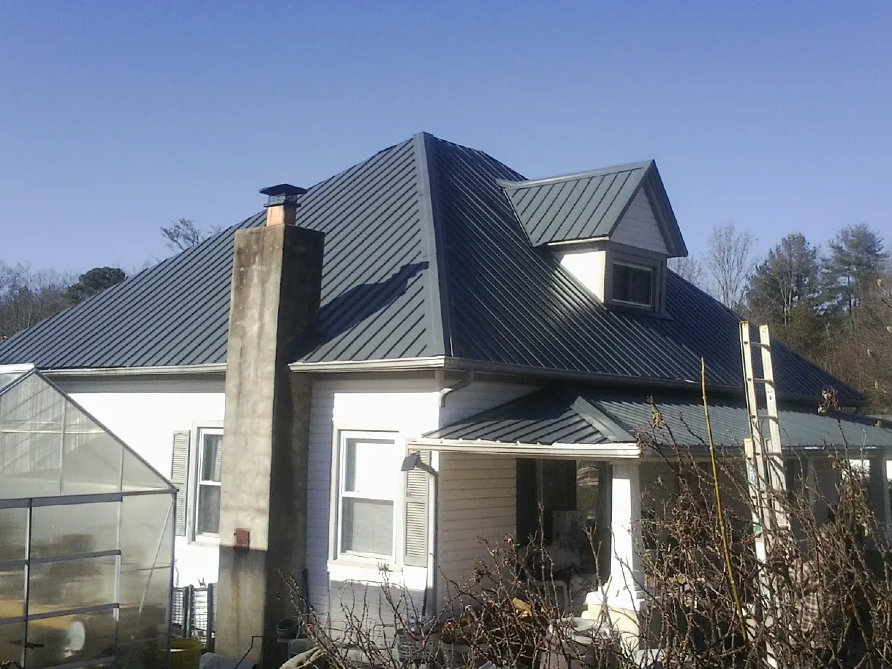 Dark blue standing seam metal roof on a white farmhouse with dormer — Slate & Tile Roof Repair by Roofing Brothers in Clifton Park