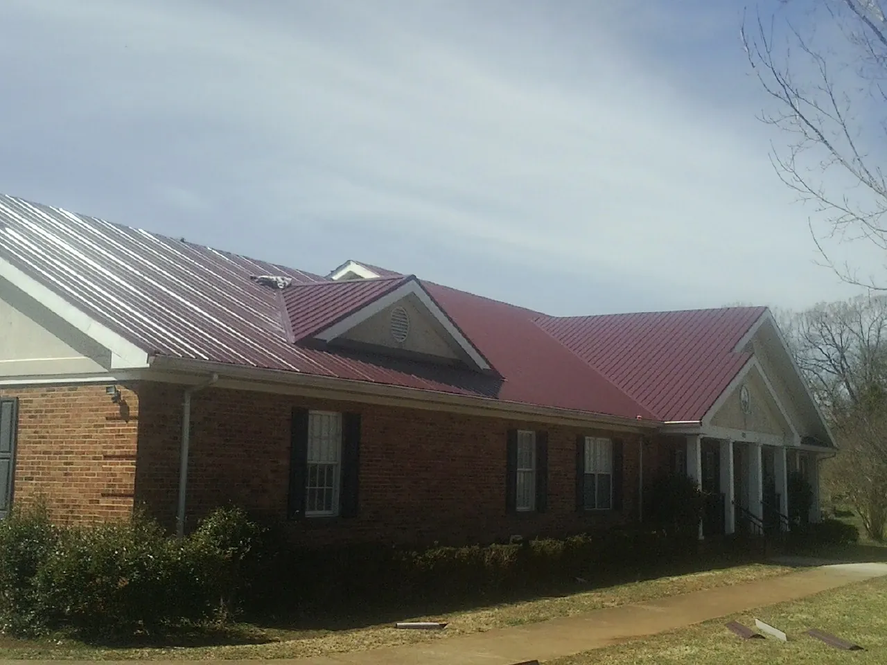 Red metal roof with gabled entries on a long brick building, from a Hail Damage Roof Repair job in Clifton Park