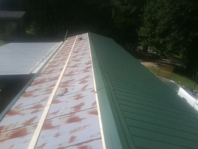 Old rusted panels beside newly installed green metal roofing — Wind Damage Roof Repair by Roofing Brothers in Clifton Park