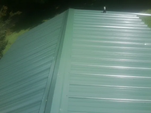 New green metal panels meeting at the ridge of a roof — Flat Roof Repair work by our crew in Clifton Park