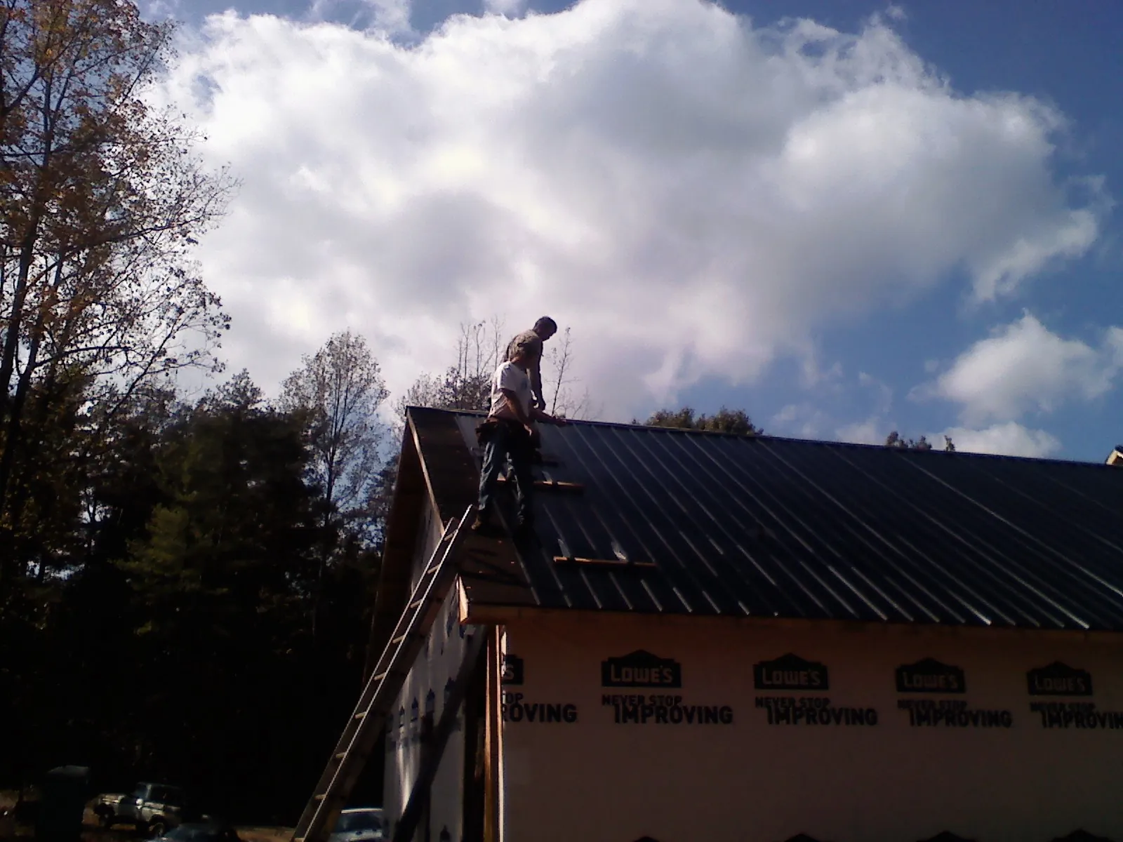 Roofer fastening dark metal panels high against a cloudy sky, from a Roof Inspection job in Clifton Park