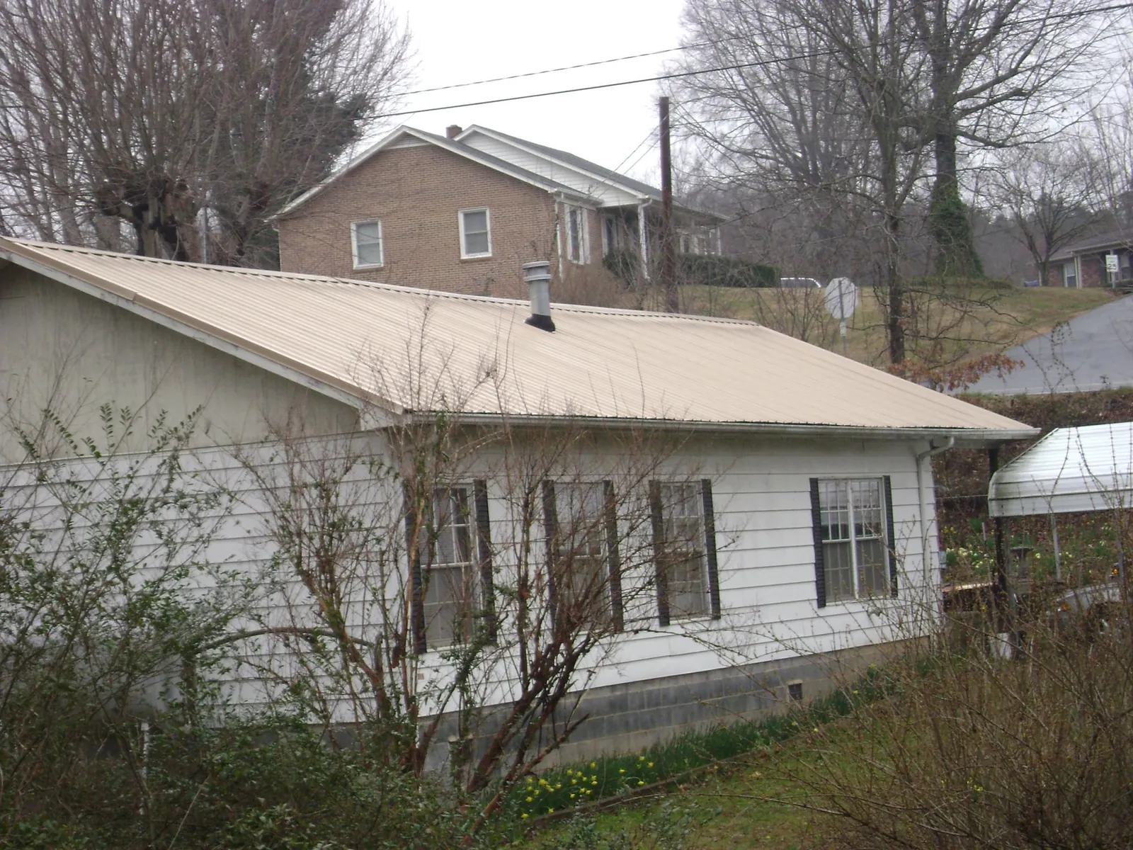 Tan metal roof on a white sided house set into a hillside — Commercial Roofing by Roofing Brothers in Clifton Park
