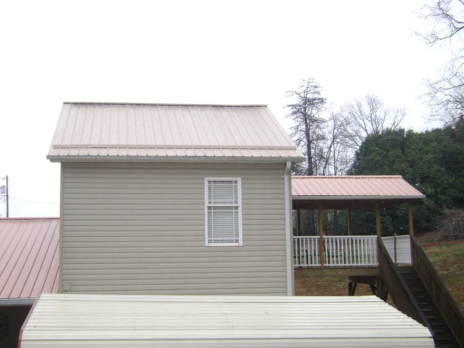 Tan metal roofs on a two story addition and attached porch, from a Roof Replacement job in Clifton Park